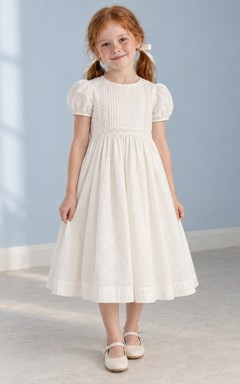 Schlichtes, schlichtes, wadenlanges, elfenbeinfarbenes Blumenmädchenkleid mit kurzen Puffärmeln, zarter Spitzenborte, Abnähern, Raffungen und Knopfleiste am Rücken.