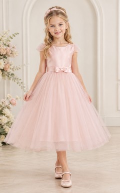 Robe de demoiselle d'honneur en tulle rose poudré, coupe trapèze, manches à volants, longueur thé, avec nœud. Idéale pour un mariage champêtre.