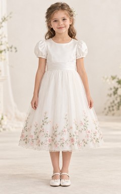Vestido de niña de flores color marfil, corte en A, manga abullonada, dobladillo bordado con motivos botánicos y lazo en la espalda.