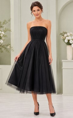 Vestido negro de tul sin tirantes, sin mangas, de corte A, largo hasta la rodilla, con pliegues.