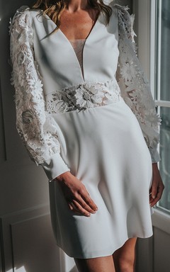 Robe de mariée courte moderne à manches longues et col en V, ornée d'appliqués et d'une découpe en forme de goutte.