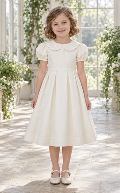 Schlichtes, elegantes Vintage-Blumenmädchenkleid in Elfenbein, knielang, mit abgerundetem, geschwungenem Kragen, kurzen Puffärmeln und kastenförmigen Falten an den Ärmelbündchen.