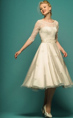 Vestido de novia de corte A, largo hasta la rodilla, con mangas ilusión, escote redondo y apliques de tul.
