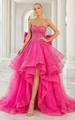 Vestido de fiesta fucsia sin tirantes con lazo de encaje, volantes en cascada, corte A asimétrico y cola de corte clásico.