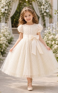 Vestido de niña de flores de tul color marfil con lunares, corte en A, manga corta, cuello redondo, fajín con lazo, largo hasta la rodilla.