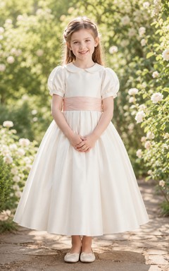 Vestido de niña de flores de satén color marfil con corte en A, mangas cortas abullonadas, escote joya y falda a la altura de la rodilla con detalles de lazos.