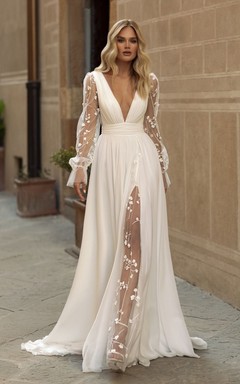 Robe de mariée vaporeuse en mousseline, manches brodées transparentes et fente haute.