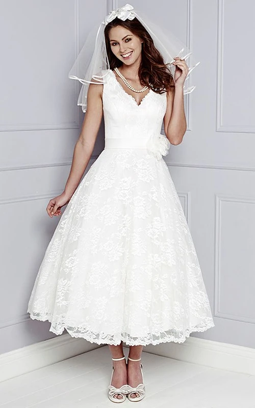 Robe de mariée courte en dentelle, sans manches, coupe trapèze, col en V, ornée d'appliqués floraux et arrivant à mi-mollet.