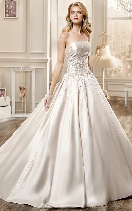 Vestido de novia largo de satén sin tirantes con adornos de pedrería y cola de capilla.
