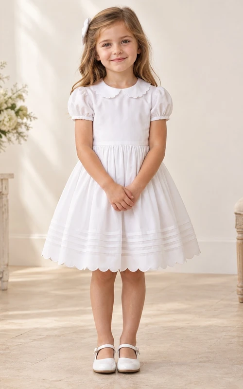 Robe de demoiselle d'honneur blanche vintage, longueur genou, col Claudine festonné, manches courtes bouffantes, ourlet arrondi froncé et boutonnée au dos.