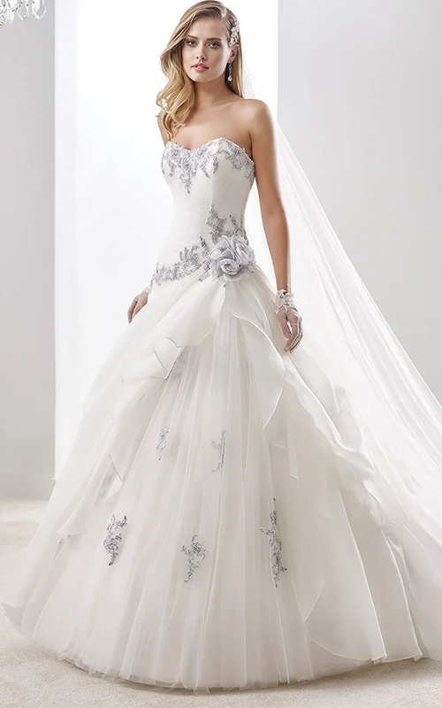 Vestido de novia de corte A con escote corazón, llamativos apliques y superposición de volantes asimétricos.