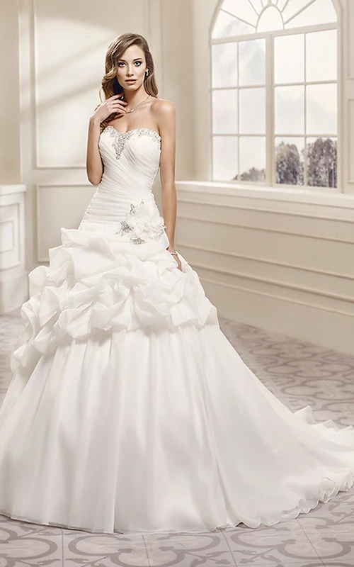 Robe de mariée longue en organza, décolleté cœur, ornée de perles et de fronces.
