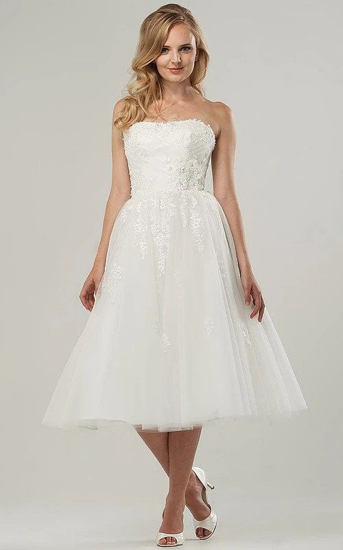 Robe de mariée courte en tulle, coupe trapèze, longueur thé, bustier croisé, ornée d'appliqués et dos corset.