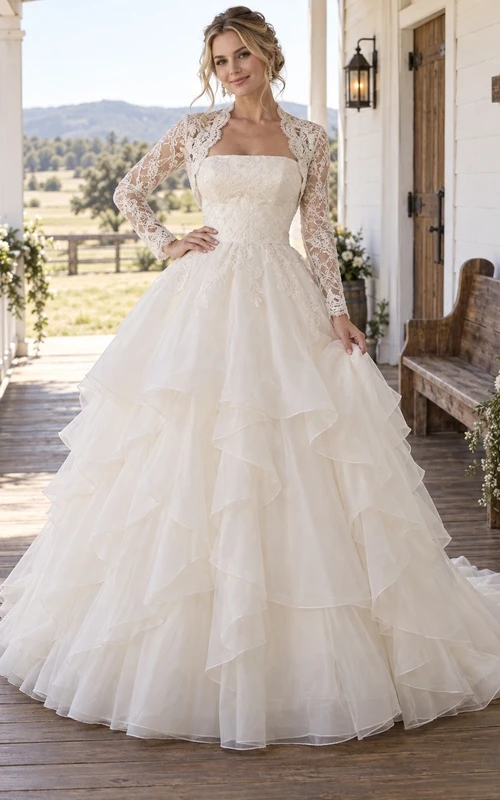 Vestido de novia de estilo bohemio campestre sin tirantes con bolero de encaje de manga larga y falda de organza en cascada.