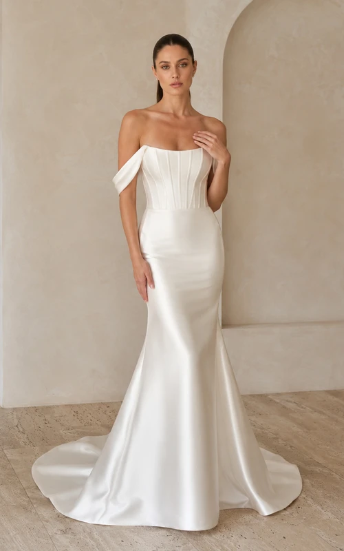 Robe de mariée minimaliste en satin discret, épaules dénudées, manches courtes, fourreau et traîne, idéale pour un mariage à destination.