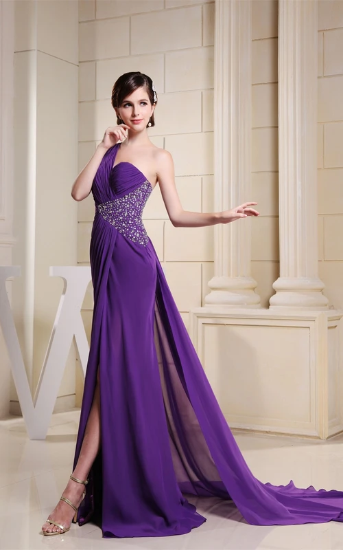 Robe asymétrique fendue sur le devant, ornée de perles et de fronces sur le côté.