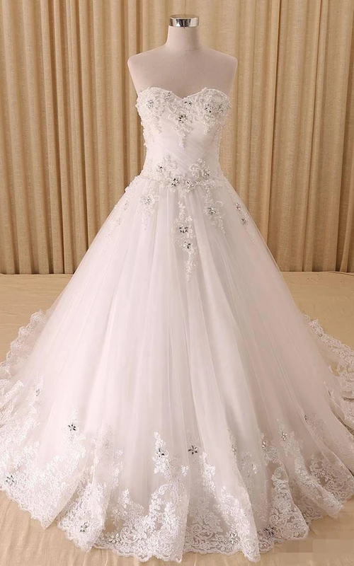 Robe trapèze à décolleté cœur, plis cloche, perles et appliques, traîne courte, fermeture éclair et laçage au dos, en mousseline, tulle, dentelle, sequins, organza, satin et taffetas.