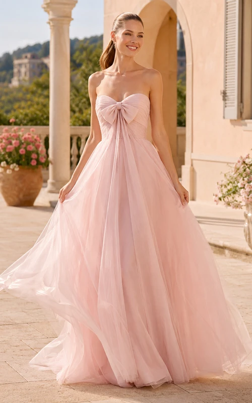Robe de mariée en tulle rose poudré à fines bretelles, décolleté cœur et nœud oversize, coupe trapèze, bretelles spaghetti et bustier.
