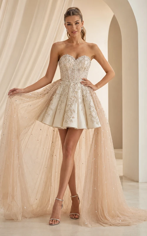 Vestido corto de quinceañera color champán, sin tirantes, con escote corazón, encaje, brillos y sobrefalda desmontable.