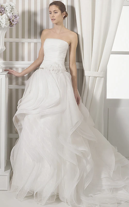 Robe de mariée simple en organza, coupe trapèze, longue, sans manches, bustier, à volants, ornée de fleurs et de fronces.