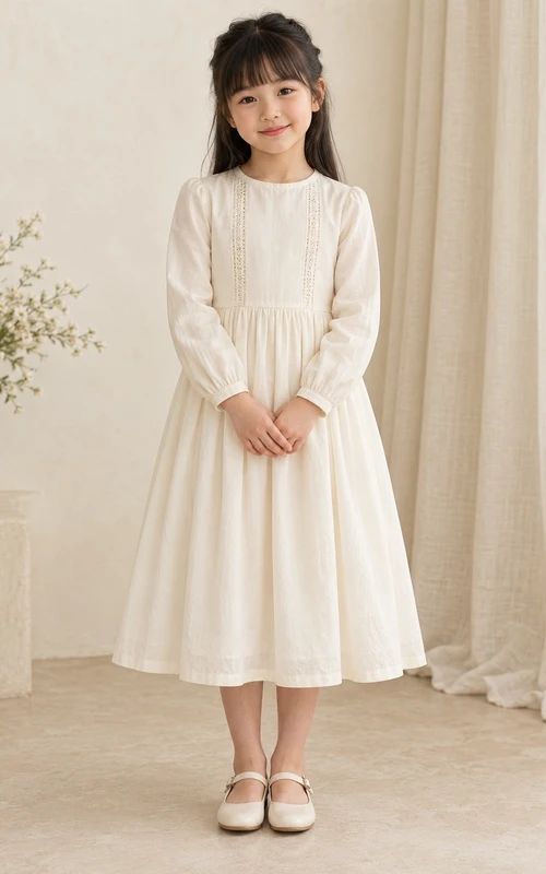 Robe de demoiselle d'honneur simple et modeste, mi-longue, couleur crème, ornée d'empiècements en dentelle fine, poignets froncés, coupe trapèze, boutonnée au dos, manches longues et ourlet arrondi.