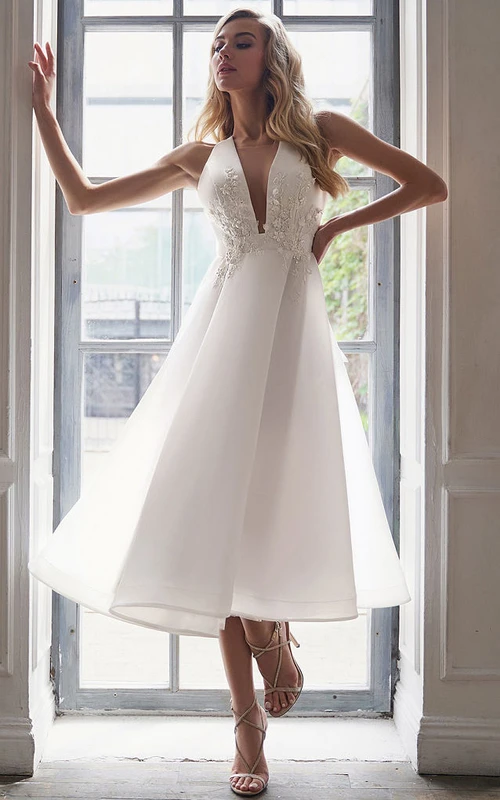Vestido de novia de satén sin mangas con escote pronunciado y largo hasta la rodilla con apliques en la parte superior.