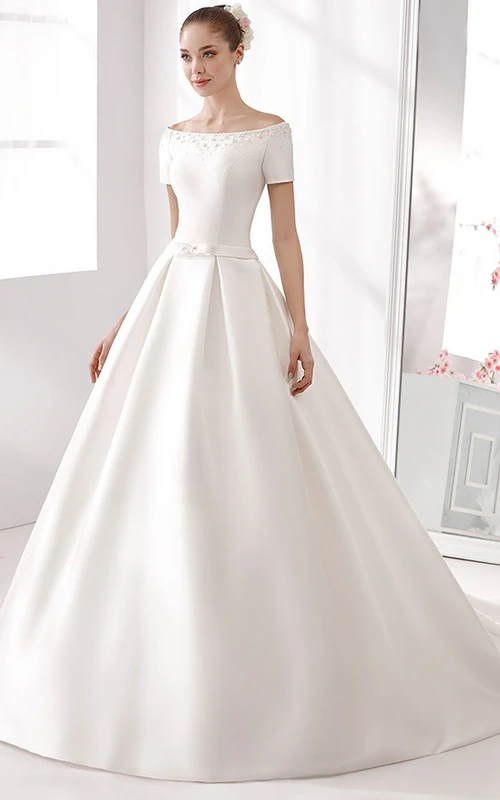 Vestido de novia de satén de corte A con hombros descubiertos, detalles de pedrería y un pequeño lazo en la faja.