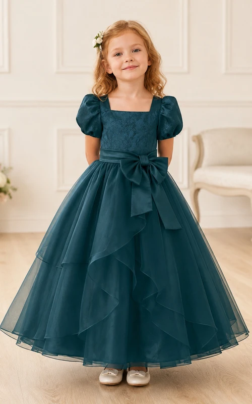 Robe de demoiselle d'honneur bleu turquoise en tulle à volants superposés, coupe trapèze, manches bouffantes et nœud.