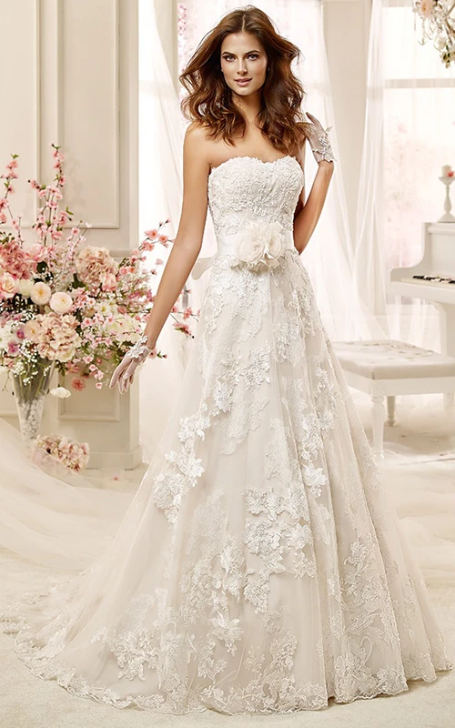 Vestido de novia palabra de honor con apliques de encaje, flores y lazo en la espalda.