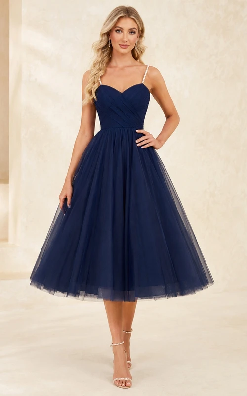 Robe de bal bleu marine en tulle, longueur thé, décolleté cœur, bretelles perlées, jupe ample et coupe trapèze.