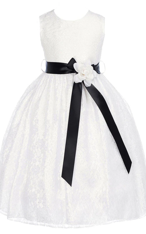 Robe de première communion sans manches en dentelle, coupe trapèze, ornée d'une fleur et d'un nœud.