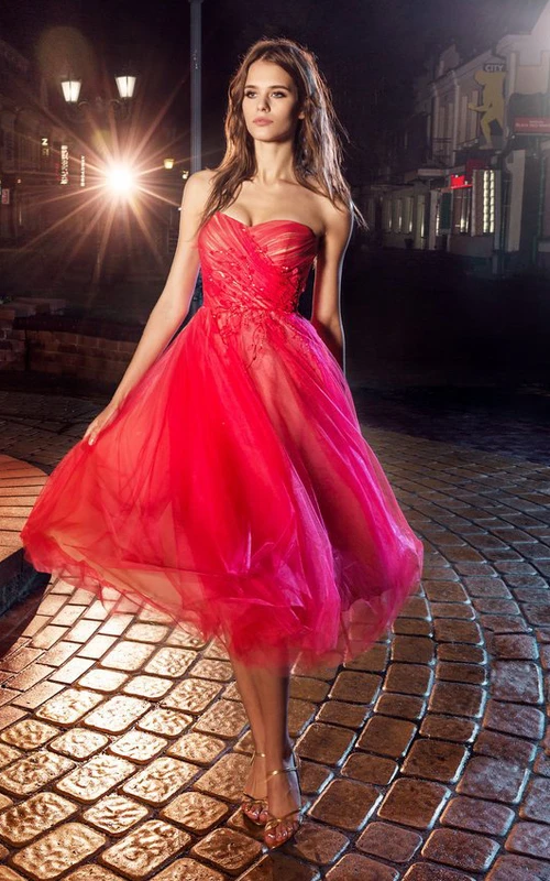 Robe bustier en tulle, longueur genou, coupe trapèze, dos nu, ornée d'un décolleté croisé et de fleurs.