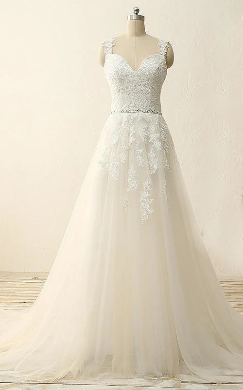 Robe trapèze à bretelles mi-longues, décolleté en V en cœur, sans manches, ornée de perles et d'appliques, avec traîne courte. Bretelles en tulle, dentelle et sequins. Satin.