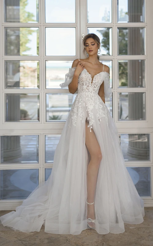 Robe de mariée en tulle et dentelle, coupe trapèze, col en V, manches chauve-souris, traîne, ornée d'appliqués et fendue sur le devant.
