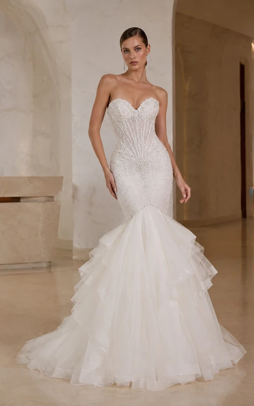 Robe de mariée sirène bustier en satin et tulle brillant, décolleté cœur et traîne à volants superposés, idéale pour une salle de bal.