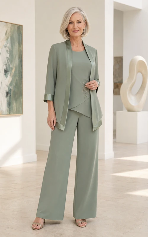 Salbeigrüner, moderner Hosenanzug für die Mutter der Braut mit weitem Bein, asymmetrischem Dreiviertel-Jäckchen mit Rundhalsausschnitt, Satinbesatz und Palazzo-Hose.