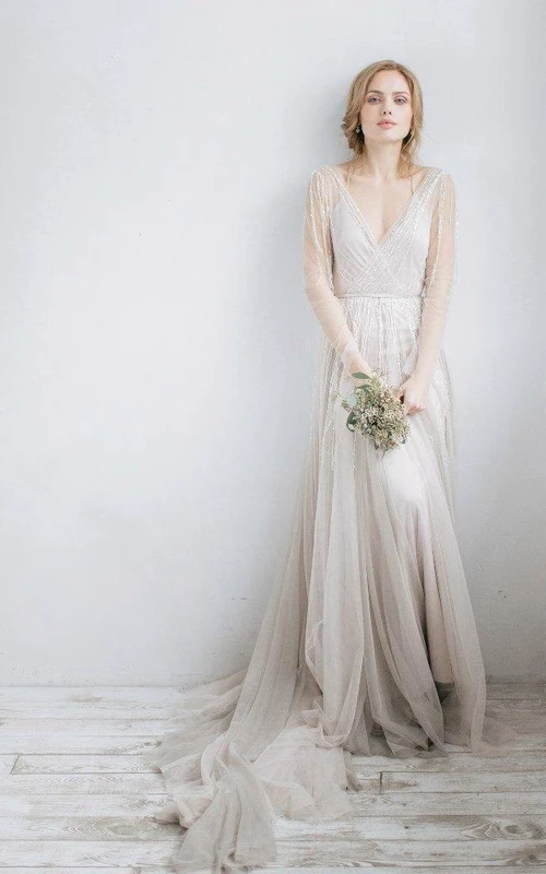 Vestido de novia de tul con escote en V y mangas largas, con efecto ilusión y detalles de pedrería.