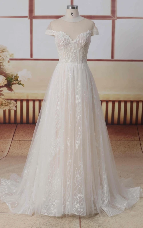 Vestido de novia de corte A con escote joya, mangas cortas de efecto ilusión, encaje y tul, espalda con efecto ilusión y pliegues.