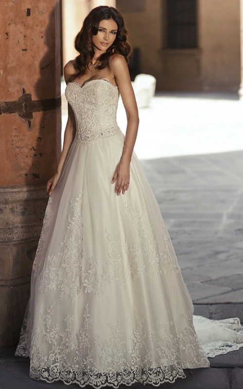 Robe de mariée longue sans manches, coupe trapèze, décolleté en cœur en dentelle appliquée, avec bijoux de taille.