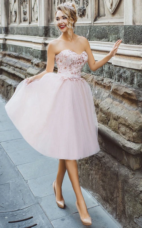 Vestido de corte A hasta la rodilla, escote corazón, sin mangas, con apliques de tul, pliegues y cordones.