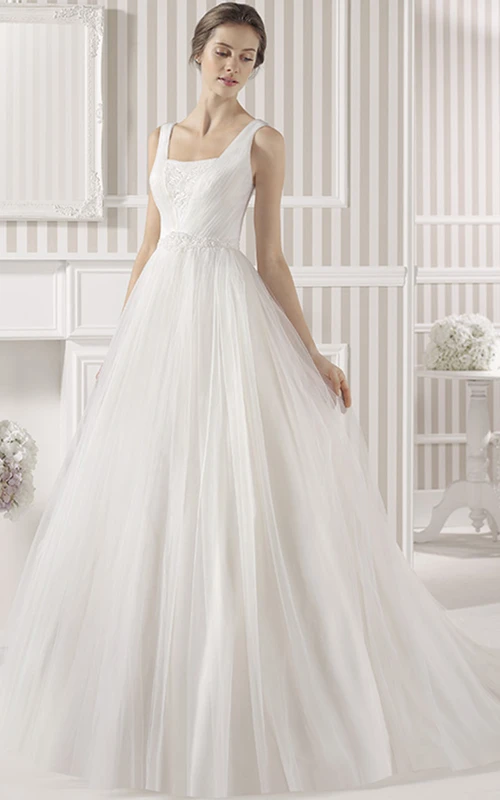 Robe de mariée maxi en tulle, style empire, sans manches, ornée d'appliqués carrés et d'une traîne courte, avec un décolleté en V plongeant.