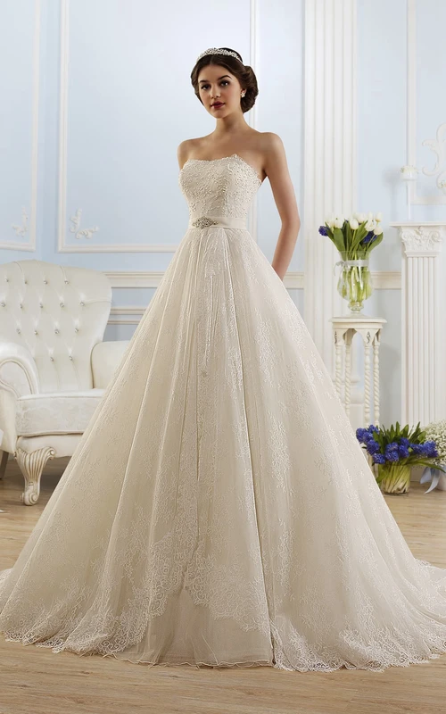 Robe longue trapèze sans bretelles, dos nu et sans manches, en dentelle, ornée de bijoux de taille et de plis.