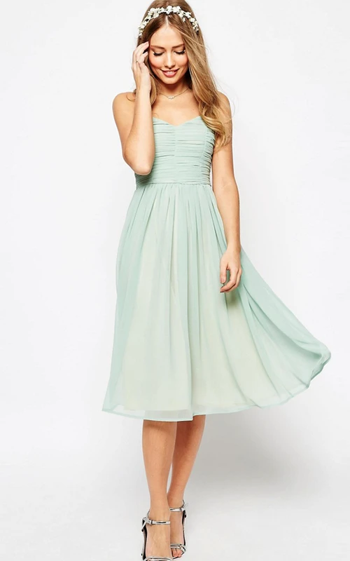 Robe de demoiselle d'honneur vert sauge, longueur thé, coupe trapèze, froncée, sans manches, en mousseline spaghetti, à fines bretelles.