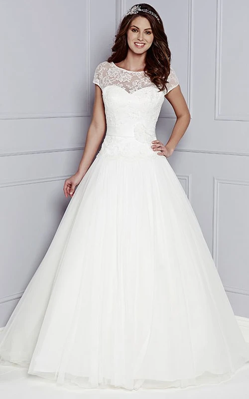 Robe de mariée en tulle et dentelle, coupe trapèze, manches courtes, longueur au sol, décolleté rond, ornée de fleurs.