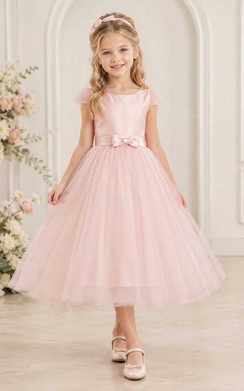 Robe de demoiselle d'honneur en tulle rose poudré, coupe trapèze, manches à volants, longueur thé, avec nœud. Idéale pour un mariage champêtre.