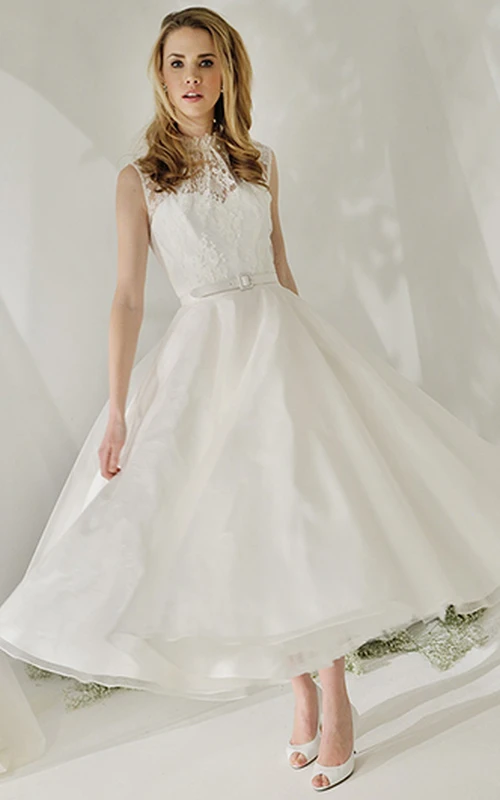 Robe de mariée trapèze en satin et dentelle, sans manches, col montant, longueur thé, dos illusion, col montant et coupe trapèze.