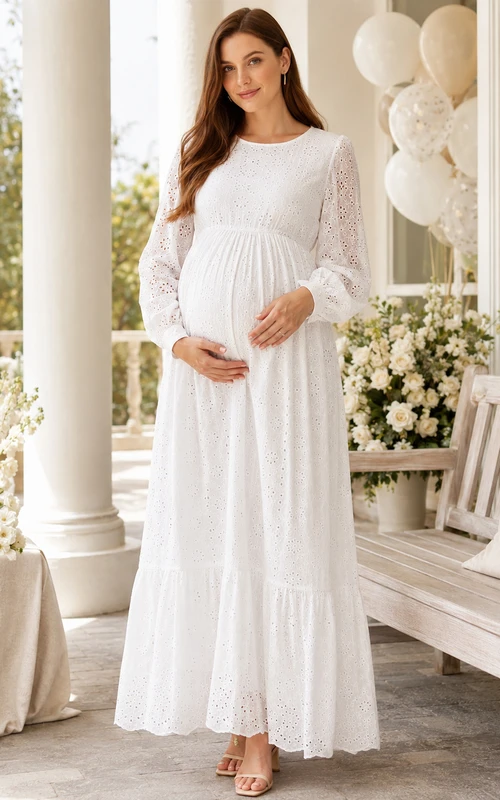 Vestido blanco de maternidad con cuello joya, manga larga, encaje calado y falda escalonada hasta el tobillo.