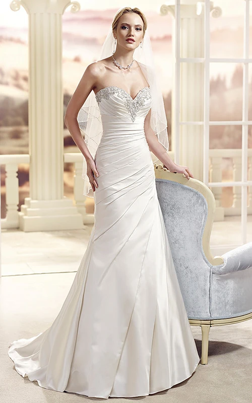 Robe de mariée longue en satin, décolleté en cœur, ornée de perles et drapée sur le côté