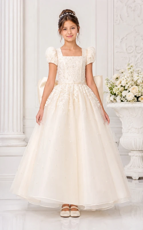 Robe de bal de première communion en tulle ivoire, col carré, manches bouffantes et nœud dans le dos.