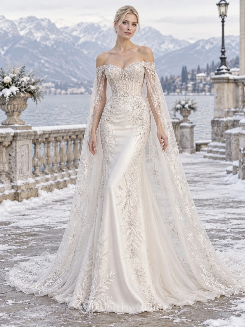 Vestido de novia romántico de invierno estilo sirena con capa transparente, bordado en plata y hombros descubiertos.